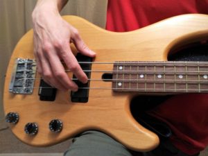picture of electric bassist right hand at the instrument, ready to pluck the strings